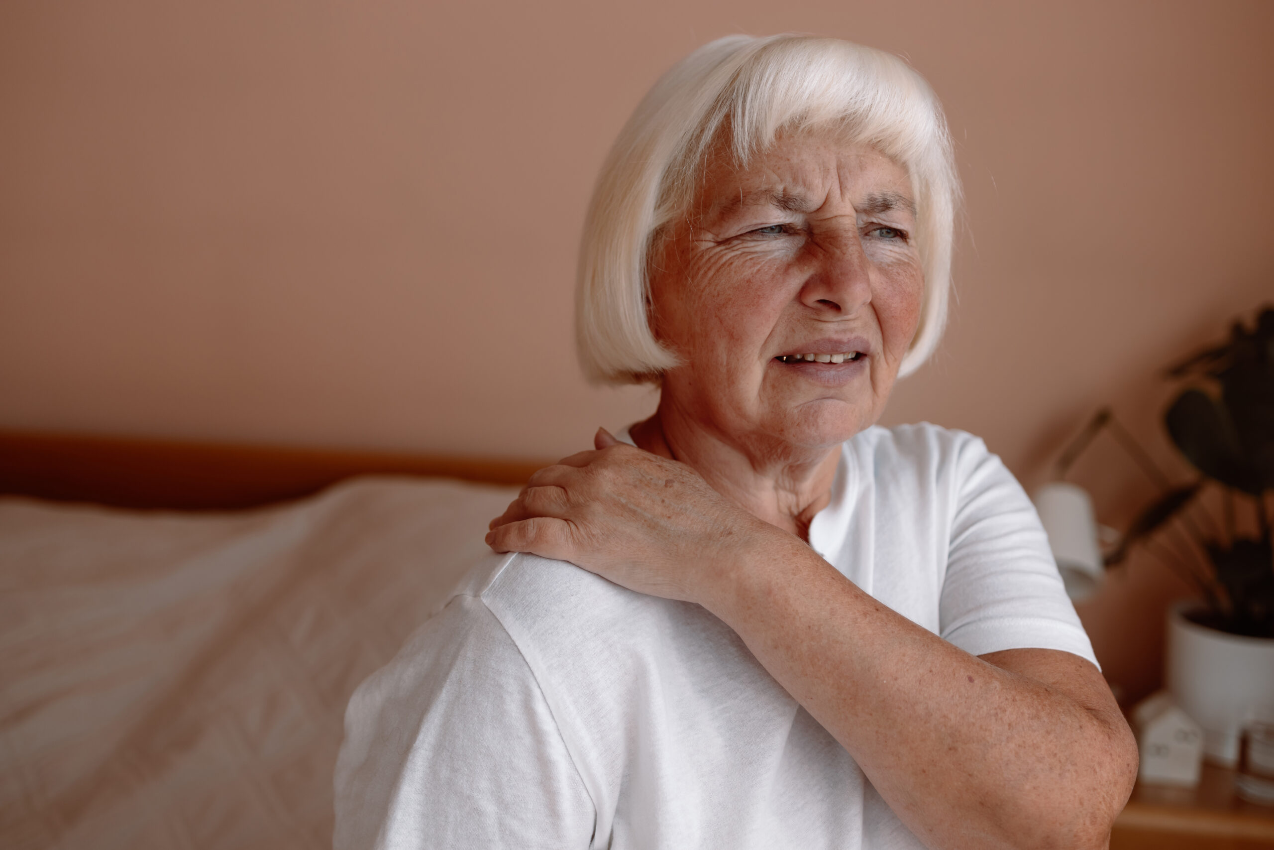 Back & Neck Pain Chiropractic 1 Senior woman with shoulder pain at home, holding her arm and wincing in discomfort