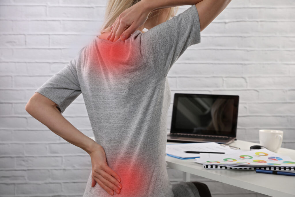 Back Pain from Poor Posture While Working at a Desk Woman with upper and lower back pain sitting at a desk, highlighting workplace posture issues