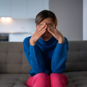 Woman sitting on a couch with hands on forehead, experiencing a migraine or severe headache