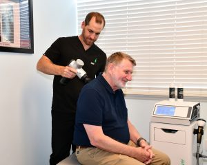 Back & Neck Pain Chiropractic 1 Dr. Bryan Wells, D.C. using percussion therapy on a patient's neck at Florida Spine Chiropractic, Vero Beach